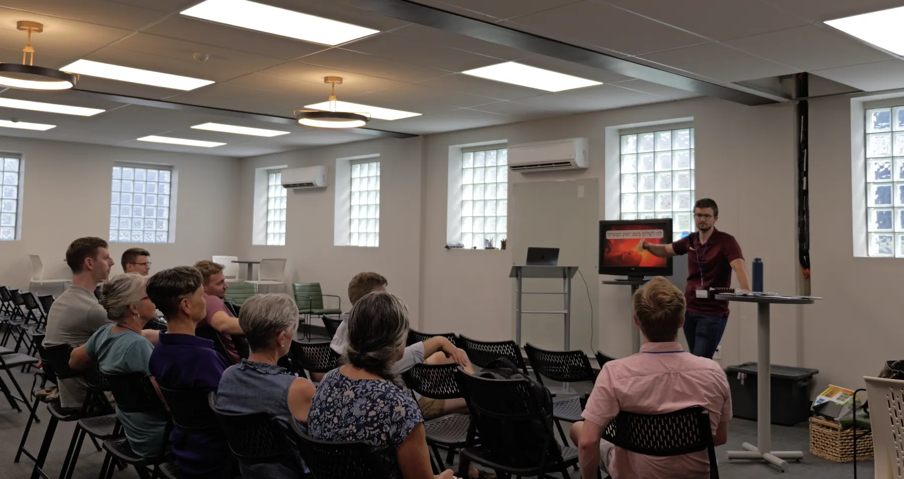 An in-person teaching session: students seated facing a screen of Hebrew text while the teacher points to the lesson